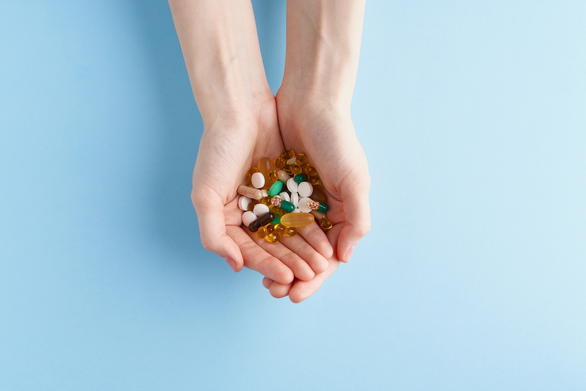 Hand with handful of scattered medicines, pills and tablets on blue background