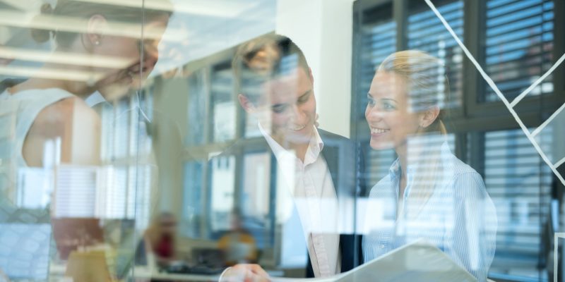Smiling business team behind glass wall in office looking at folder